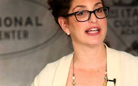 Woman with glasses speaking during a presentation at a cultural center event. - Olive Oil Times