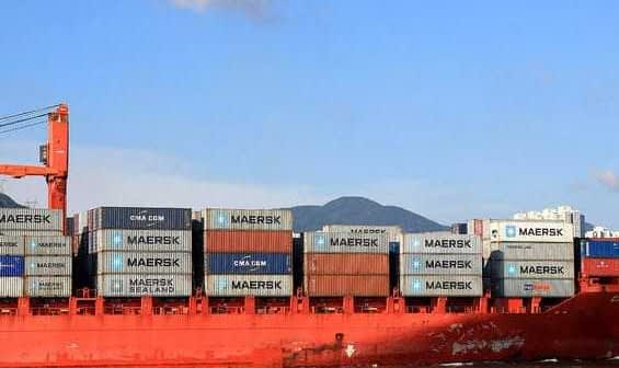 Red cargo ship loaded with shipping containers, including Maersk branding, on the water. - Olive Oil Times