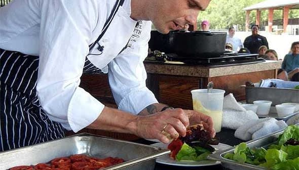 Chef in a white coat arranging salad ingredients on a plate during a cooking demonstration. - Olive Oil Times
