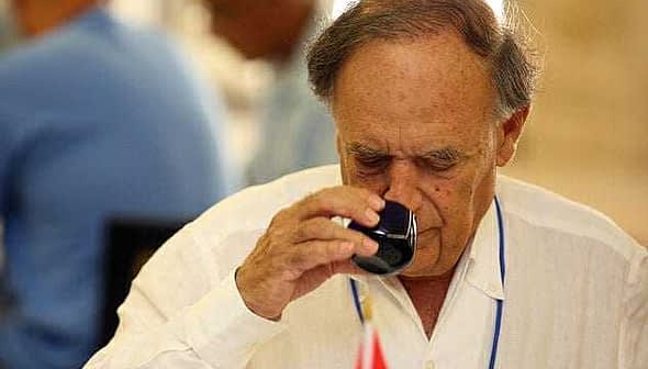 An older man in a white shirt tasting olive oil from a small glass cup. - Olive Oil Times