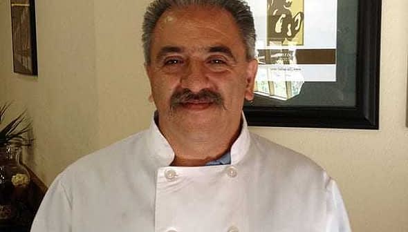 A chef wearing a white coat with a UC Davis logo, smiling in a well-lit indoor setting. - Olive Oil Times
