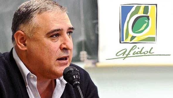 A man speaking into a microphone at an event with the Afidol logo in the background. - Olive Oil Times