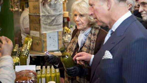 Charles and Camilla inspecting a bottle of olive oil at a market stall. - Olive Oil Times