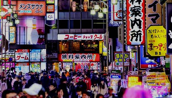 Busy street in Tokyo filled with people and illuminated neon signs in various colors and languages. - Olive Oil Times