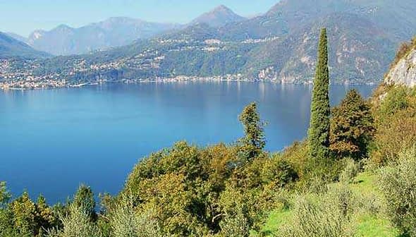 A scenic view of a lake surrounded by mountains and trees under a clear blue sky. - Olive Oil Times