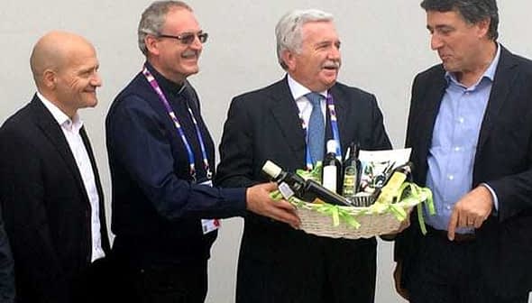 Four men standing together, one presenting a basket filled with olive oil products. - Olive Oil Times