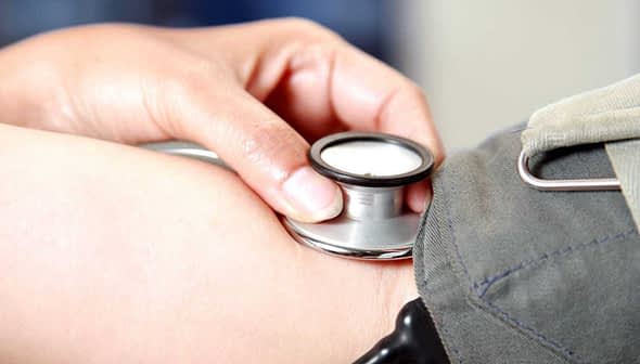 A healthcare professional using a stethoscope on a patient's arm during a medical examination. - Olive Oil Times