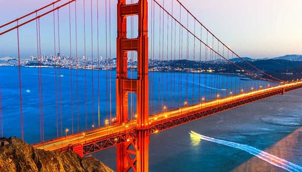 Golden Gate Bridge illuminated at sunset with a city skyline in the background. - Olive Oil Times