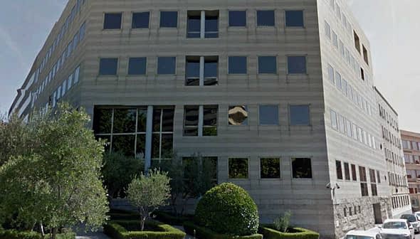 Contemporary office building featuring large glass windows and a landscaped area. - Olive Oil Times