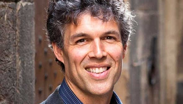 A man with curly hair and a friendly smile, wearing a dark blazer and blue shirt. - Olive Oil Times