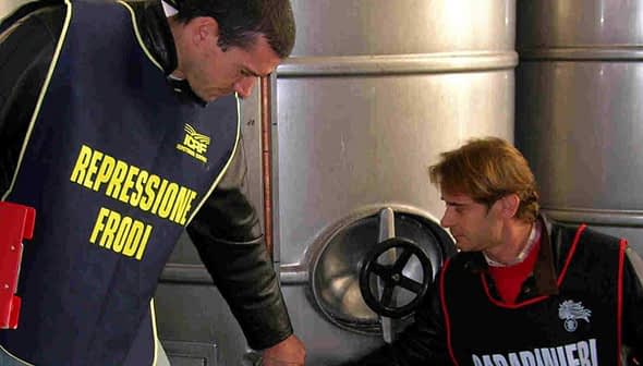 Two inspectors in vests examining olive oil storage tanks in a facility. - Olive Oil Times