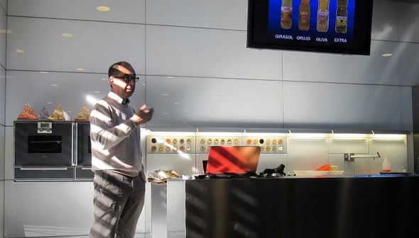 A person giving a presentation in a modern kitchen with a screen displaying various oil types. - Olive Oil Times