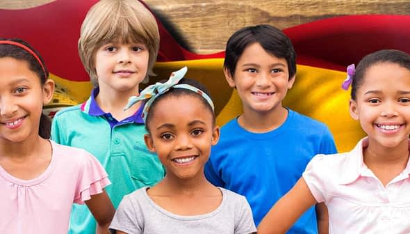 Five children posing together in front of a Spanish flag background, smiling and wearing casual clothing. - Olive Oil Times