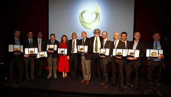 Group of individuals holding awards during a ceremony with a backdrop display. - Olive Oil Times