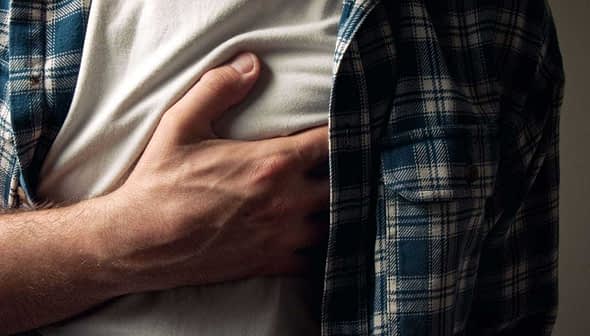 Individual in a plaid shirt holding their chest with a pained expression. - Olive Oil Times