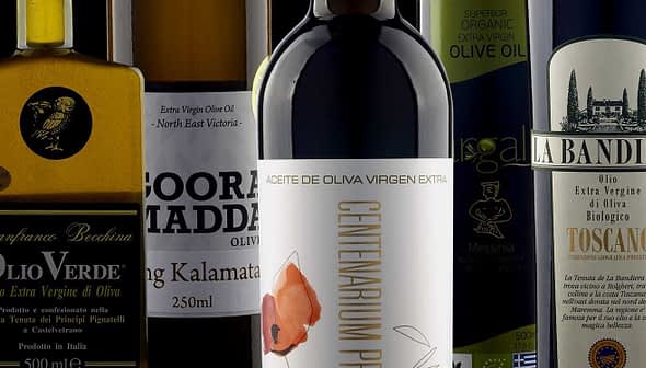 A collection of olive oil bottles featuring different brands and labels on a neutral background. - Olive Oil Times