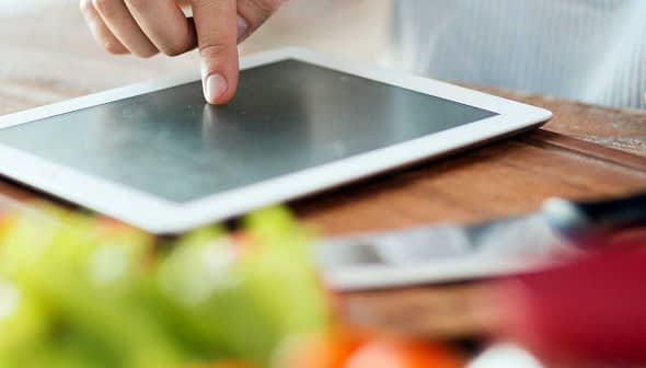 A person pointing at a tablet screen while preparing food in a kitchen setting. - Olive Oil Times