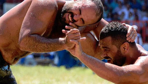 Two male wrestlers in a Greco-Roman wrestling match, grappling on a grassy field. - Olive Oil Times