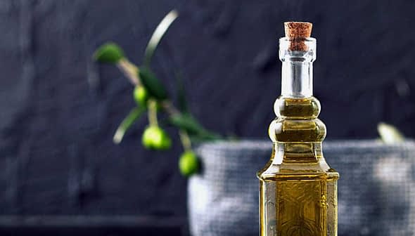 A glass olive oil cruet with a cork stopper, featuring a smooth design and filled with olive oil. - Olive Oil Times