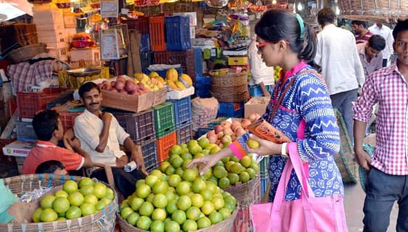 A woman selecting limes from a basket in a busy fruit market with people around her. - Olive Oil Times