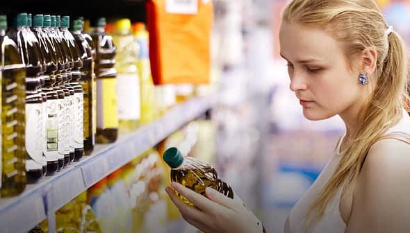 A woman inspecting a bottle of olive oil while shopping in a supermarket aisle. - Olive Oil Times