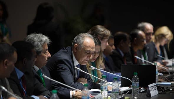 Group of officials seated at a conference table during a meeting, with a speaker addressing the group. - Olive Oil Times
