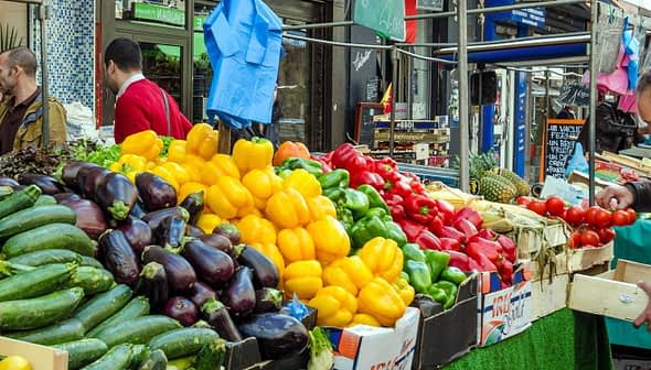 A vibrant display of various vegetables including peppers, zucchini, and tomatoes at a market stall. - Olive Oil Times
