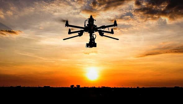 Silhouette of a drone flying against a sunset with clouds in the sky. - Olive Oil Times