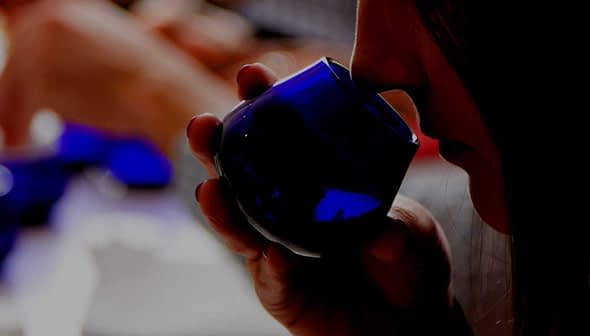 Individual holding a blue glass container while smelling olive oil during a tasting session. - Olive Oil Times