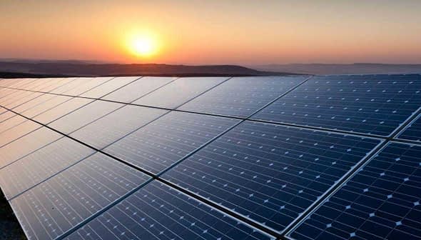 Row of solar panels reflecting sunlight during sunset with a distant horizon. - Olive Oil Times