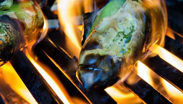 Green peppers being grilled on a barbecue grill with flames visible. - Olive Oil Times