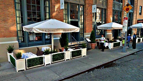 Outdoor dining area with white umbrellas and tables at Fig & Olive restaurant. - Olive Oil Times
