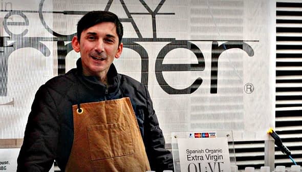 Man wearing an apron standing behind a table at an olive oil tasting event. - Olive Oil Times