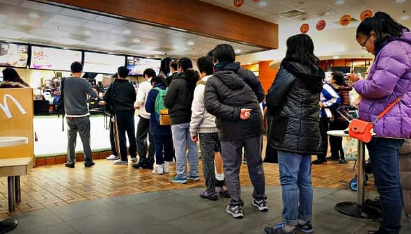 A group of people standing in line at a McDonald's restaurant waiting to order. - Olive Oil Times