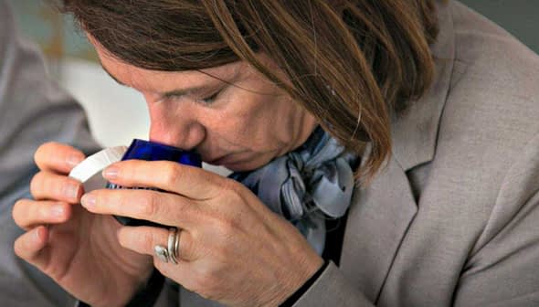 Individual smelling a small blue container during an olive oil tasting session. - Olive Oil Times