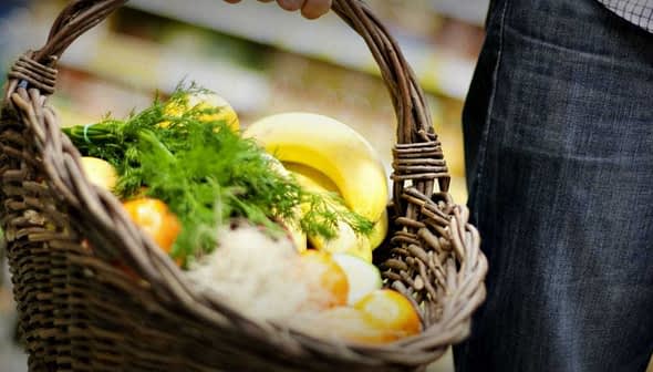 A person holding a woven basket filled with various fresh fruits and vegetables. - Olive Oil Times