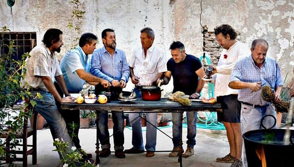A group of men gathered around a table preparing food outdoors in a rustic setting. - Olive Oil Times