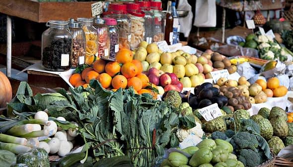 A market stall displaying a variety of fresh fruits and vegetables including oranges, apples, and greens. - Olive Oil Times