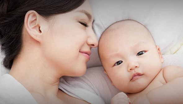A mother and her baby lying close together, both looking at the camera with soft expressions. - Olive Oil Times