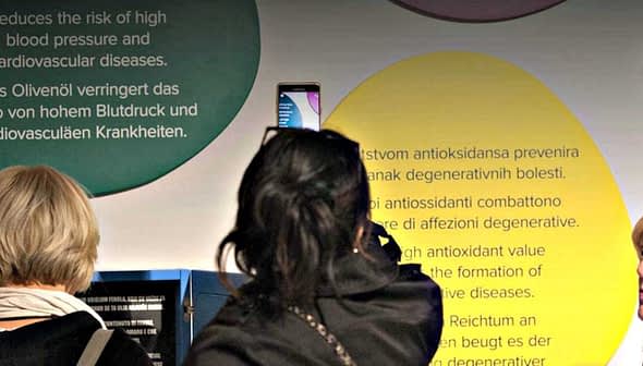 Two women viewing informational displays about health benefits of olive oil at an exhibit. - Olive Oil Times