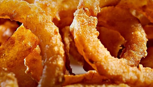 Close-up of crispy fried onion rings arranged in a circular pattern. - Olive Oil Times