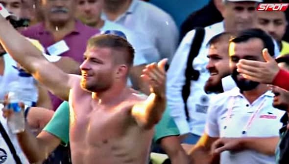 A shirtless wrestler celebrating with a crowd of spectators after a match. - Olive Oil Times