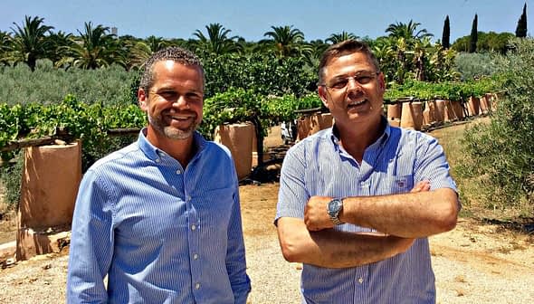 Two men standing in an olive grove, smiling and posing for the camera. - Olive Oil Times
