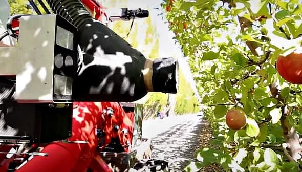 Close-up of a fruit harvesting machine positioned near apple trees in an orchard. - Olive Oil Times