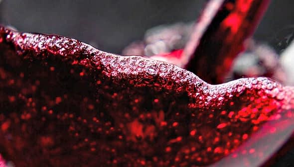 Close-up of red wine being poured into a glass, showcasing bubbles and liquid movement. - Olive Oil Times