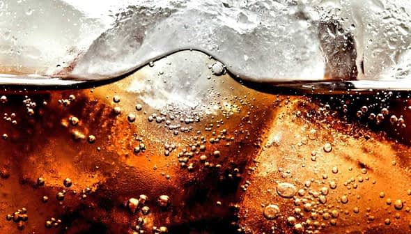 Close-up image of a carbonated beverage with ice cubes and bubbles visible in the liquid. - Olive Oil Times