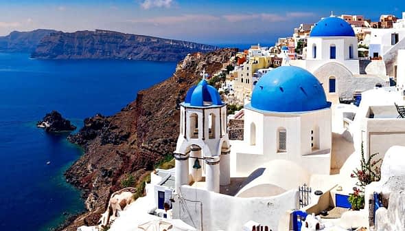 View of Santorini island featuring white buildings with blue domes against the sea. - Olive Oil Times