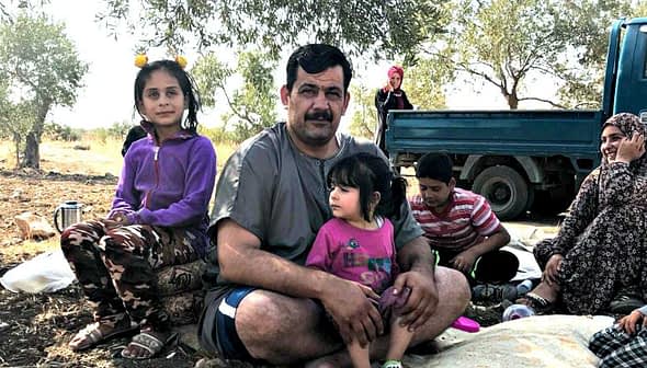 A family sitting together during a break from harvesting, with children and adults in casual clothing. - Olive Oil Times