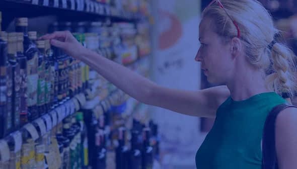 Woman reaching for a bottle of olive oil on a supermarket shelf filled with various oils. - Olive Oil Times