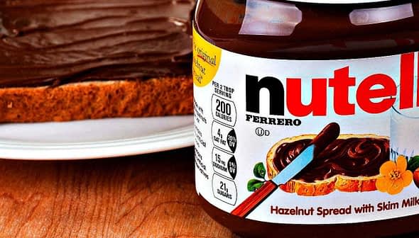 Jar of Nutella hazelnut spread next to a slice of bread topped with the spread. - Olive Oil Times
